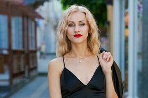mooi blond vrouw met rood lippenstift in zwart top en leggings poseren Aan straat in de stad foto