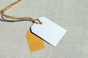 twee rechthoekig tags met een touw Aan een grijs kleding stof. blanco etiket mockup met prijs label foto