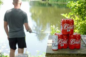 budweiser knop bier blikjes pak Aan oud tafel en visser Bij rivier- Aan achtergrond foto