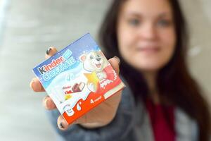 jong vrouw shows kinder chocola snoep doos in gekleurde inpakken. kinder chocola door Italiaans banketbakkerij fabrikant Ferrero foto