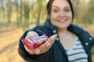 Charkov, Oekraïne - oktober 21, 2019 jong meisje passeert een uitrusting kat chocola bar in een herfst park. de manifestatie van vriendelijkheid, behandelen met snoepgoed foto