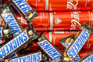 grinnikt chocola bars in bruin omhulsel leugens Aan rood coca cola blik blikjes dichtbij omhoog. beroemd drinken en chocola Product foto