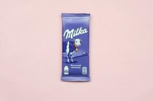 milka chocola tablet in klassiek paars omhulsel Aan pastel roze achtergrond. milka is merk van chocola confectie is ontstaan in Zwitserland in 1901 foto