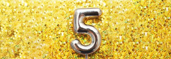 vijf jaren verjaardag feest. aantal vijf met gouden confetti in het formulier van sterren Aan geel achtergrond foto