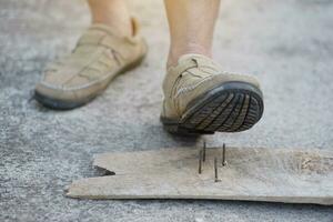 detailopname Mens slijtage schoenen is stepping Aan roestig metaal nagel Aan hout. concept, onveilig , risico voor gevaarlijk tetanus. worden voorzichtig en kijken in de omgeving van gedurende wandelen Aan de verdieping of risico plaatsen. ongeluk foto