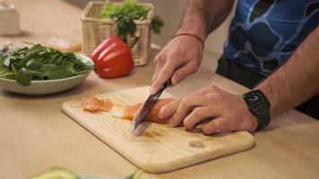 handen kookt close-up. de chef-kok snijdt met een mes een rode vis, gerookte zalm op een houten snijplank.
