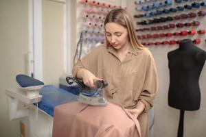 vrouwelijke kleermaker die strijkstoom gebruikt. de stoomgenerator. modeontwerper strijkt stof in zijn atelier