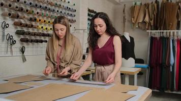 twee naaisters werken met een doek en een krijt op een tafel. vrouwelijke naaister gebruikt krijt op de patrooncontour op textiel, in atelier. professionele kleermaker, modeontwerper bij naaiatelier.