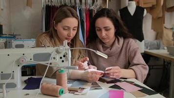 twee modeontwerpers kijken naar stofstalen bij de naaimachine in een naaiatelier