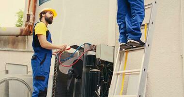 bekwaam deskundige Holding elektrisch macht boren stepping naar beneden van vouwen ladder na afwerking onderhoud op het dak hvac systeem terwijl collega assembleert verdeelstuk meters naar controleren freon niveaus foto