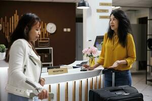 Aziatisch reizigers aankomen in knus hotel lobby Aan hun vakantie, ervan uitgaand naar krijgen onderhoud van receptioniste. nieuw toevlucht gasten aan het wachten voor conciërge naar helpen met reservering foto