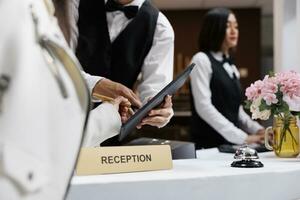 Aziatisch mannetje receptioniste Bij hedendaags hotel helpt klant teken registratie het formulier. reservering hotel kamer Bij luxueus toevlucht door gaan door bezoeker register Bij voorkant bureau foto