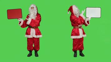 heilige Nick Holding toespraak bubbel rood aanplakbord terwijl hij draagt feestelijk traditioneel kostuum en hoed. de kerstman belichaming tonen karton icoon voor advertentie, vol lichaam groene scherm. foto