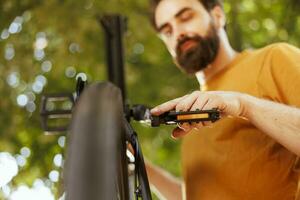 fit en actief mannetje fietser bevestiging fiets pedaal veilig voor buiten wielersport. toegewijd sportief Mens het uitvoeren van fiets onderhoud vakkundig repareren fiets zwengel arm met essentieel werk hulpmiddel. foto