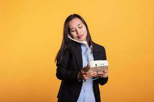 Aziatisch vrouw in formeel pak pratend Aan vaste telefoon telefoon telefoongesprek, gebruik makend van telefoon met koord staand over- geel achtergrond. zelfverzekerd jong volwassen gebruik makend van kantoor retro telefoon hebben afgelegen discussie in studio foto