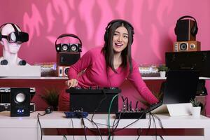 Aziatisch musicus spelen elektronisch muziek- gebruik makend van professioneel draaitafels terwijl staand Bij dj tafel in studio over- roze achtergrond. artiest aan het doen prestatie Bij nachtclub met audio uitrusting foto