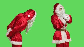 Mens in rood pak cheques polshorloge naar zien tijd, poseren over- groene scherm achtergrond. zelfverzekerd persoon vervelend de kerstman claus feestelijk kostuum naar verspreiding Kerstmis geest, vieren winter vakantie. foto