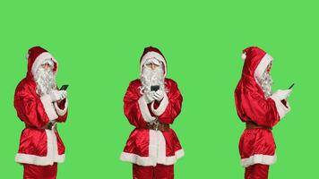 vader Kerstmis zoeken voor geschenk ideeën Aan smartphone, gebruik makend van online browser naar verspreiding Kerstmis positiviteit. de kerstman claus in pak Holding mobiel pohne over- groene scherm achtergrond, vakantie evenement. foto
