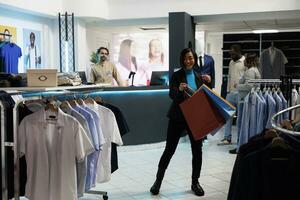 kleding op te slaan vrolijk glimlachen klant presentatie van boodschappen doen Tassen met aankopen en dansen. gelukkig opgewonden Aziatisch vrouw draag- papier pakketjes na buying kleding in winkel foto