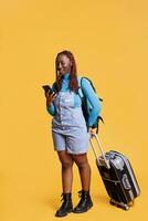 Afrikaanse Amerikaans meisje sms'en berichten en draag- trolley Tassen in studio, hebben pret Aan vakantie reis. vrouw reiziger browsen online app Aan mobiel telefoon website, vakantie reis. foto