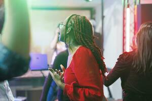 vrouw dansen met vrienden terwijl feesten Aan dansvloer met schijnwerpers in nachtclub. jong Afrikaanse Amerikaans meisje in rood blouse hebben pret en genieten van discotheek in club foto