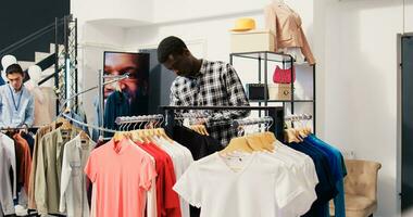Afrikaanse Amerikaans Mens controle rek met nieuw mode verzameling, analyseren handelswaar materiaal in kleding op te slaan. shopaholic cliënt boodschappen doen voor modieus kleren in modern winkel foto