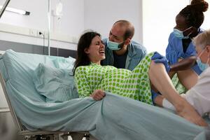 vrouw hebben pijnlijk weeën gedurende arbeid, medisch team levering baby gedurende keizersnede chirurgie in ziekenhuis afdeling. geduldig met zwangerschap voortvarend voor kind in moederschap kliniek foto