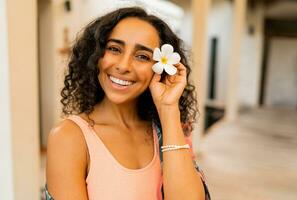 dichtbij omhoog portret van mooi vrouw met tropisch bloem in hand- poseren in luxe spa hotel. spa en lichaam zorg concept. foto