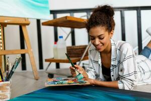 vrouw schilder leugens Aan de verdieping in de buurt canvas en tekening. artiest studio interieur. tekening benodigdheden, olie verven, artiest borstels, canvas, kader. creatief concept. foto