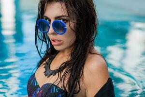 mode portret van sensueel braziliaans vrouw in zonnebrillen poseren in zwembad , vervelend boho ketting. foto