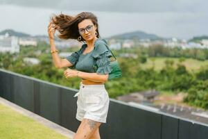 brunette vrouw in modieus Bijsnijden blouse met bladerdeeg mouw poseren in luxe hotel Aan de dak top. foto