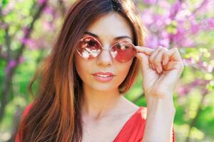 buitenshuis voorjaar dichtbij omhoog portret van romantisch brunette vrouw genieten van bloemen in zonnig bloeiend tuin. foto