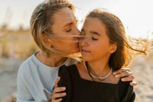 mooi blond moeder en brunette dochter poseren Aan de strand in warm zonsondergang licht. gelukkig familie resting Bij strand in zomer. foto