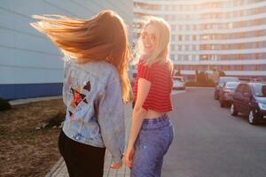 twee blij Dames hebben pret buitenshuis. elegant jeans jasje met afdrukken. stedelijk achtergrond . foto