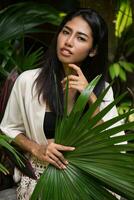 mooi Aziatisch meisje poseren in tropisch tuin, Holding groot palm blad. foto