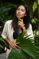 mooi Aziatisch meisje poseren in tropisch tuin, Holding groot palm blad. foto