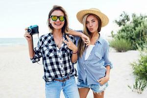 gelukkig vrienden twee mooi Dames op zoek Bij camera , Holding foto camera Aan de strand.