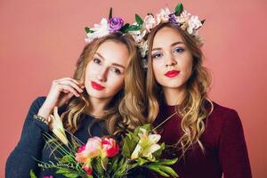 dichtbij omhoog studio portret van twee jong mooi blond Dames in voorjaar bloemen toorn , verbazingwekkend golvend lang kapsel , helder maken omhoog, op zoek Bij camera. foto