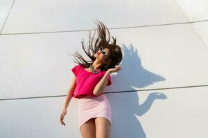 modieus brunette vrouw in zomer kleren en zonnebril poseren over- wit stedelijk achtergrond. dansen en hebben plezier. foto