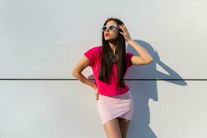 elegant vrouw in zomer kleren en zonnebril poseren over- wit stedelijk achtergrond. foto