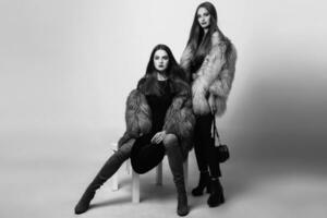 twee mooi mode modellen in winter kleren bont poseren Aan grijs achtergrond. vervelend elegant pluizig jas , zwart jeans, avond jurk en hoed. zwart en wit. foto