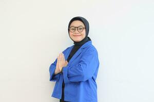 mooi jong Aziatisch moslim vrouw, vervelend bril en blauw blazer met namaste gebaar terwijl glimlachen foto