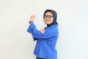 mooi jong Aziatisch moslim vrouw, vervelend bril en blauw blazer met sterk gebaar door hijs- haar armen en spieren foto