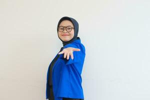 jong mooi Aziatisch moslim vrouw, vervelend bril en blauw blazer Holding iets uit Leuk vinden advertentie of kopiëren ruimte terwijl glimlachen foto