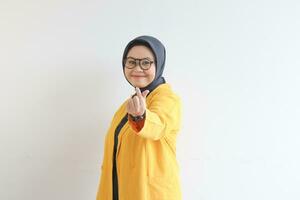 mooi jong Aziatisch moslim vrouw, vervelend bril en geel blazer gebaren Koreaans liefde teken terwijl glimlachen foto