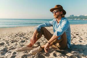 jong aantrekkelijk hipster Mens zittend Aan strand door zee Aan zomer vakantie foto