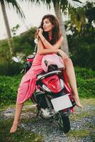 jong elegant sexy mooi vrouw in roze jurk Aan scooter motor tropisch vakantie foto