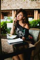 jong elegant mooi vrouw zittend Bij tropisch toevlucht cafe foto