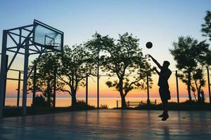 zwart Mens aan het doen sport, spelen basketbal Aan zonsopkomst, jumping silhouet foto