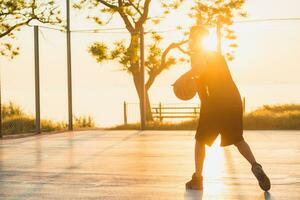 zwart Mens aan het doen sport, spelen basketbal Aan zonsopkomst, actief levensstijl, zonnig zomer ochtend- foto